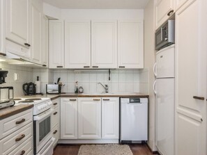 Une cuisine de taille réduite avec des meubles blancs, une cuisinière, un lave-vaisselle et un four à micro-ondes.