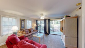 A living room with a plaid sofa, a red armchair, a glass coffee table, and a wooden cabinet.