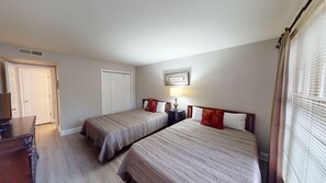 Een hotelkamer met twee eenpersoonsbedden, een houten dressoir, een bureau en een lijst aan de muur.
