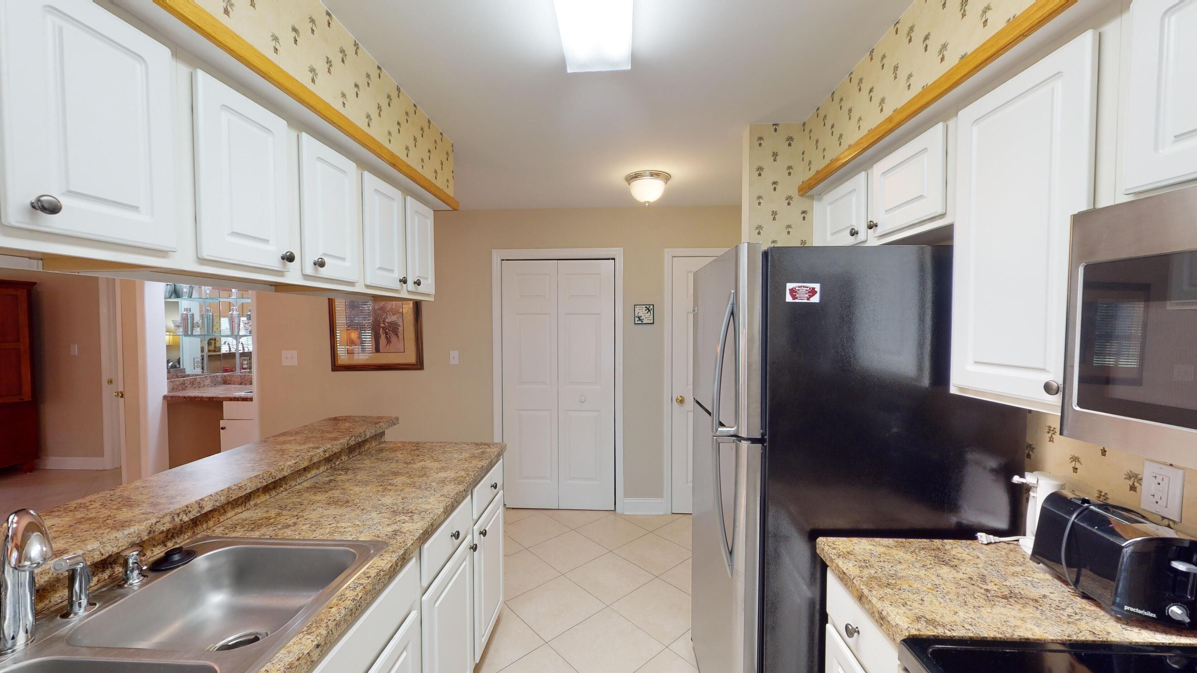 A kitchen with white cabinets, granite countertops, a black refrigerator, and a stainless steel sink.