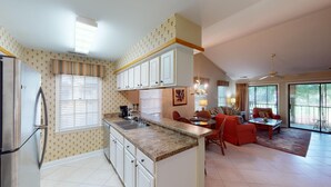 A spacious kitchen with a central island, a dining area with a red sofa, and a large sliding glass door leading to a balcony. - Golf Course Charm Pawleys Getaway (Pawleys Island)