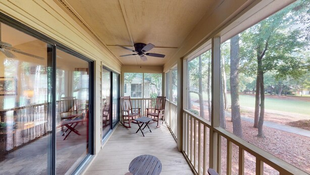 A covered porch with a ceiling fan, sliding glass doors, and a view of a residential area with trees and a road. - Golf Course Charm Pawleys Getaway (Pawleys Island)