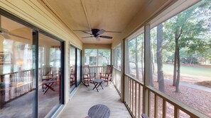 Une véranda couverte avec un ventilateur de plafond, des portes-fenêtres coulissantes et une vue sur un quartier résidentiel, avec des arbres et une route.