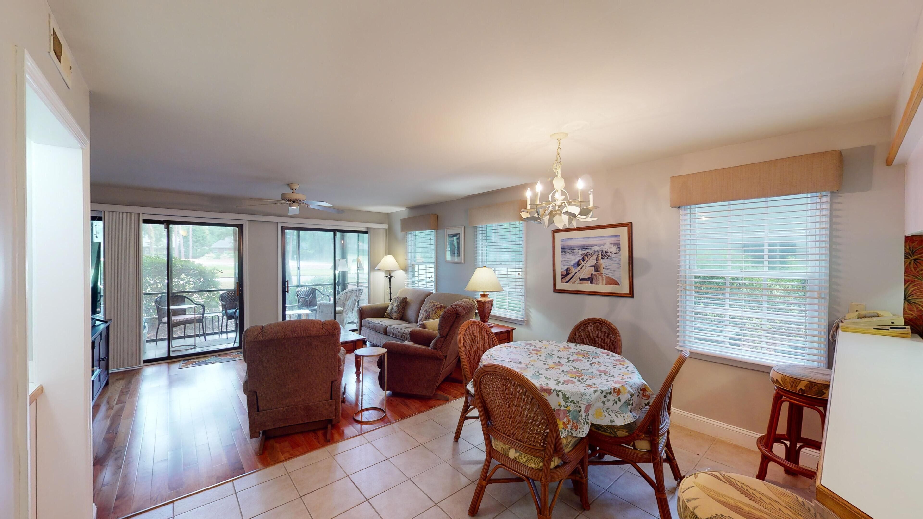A spacious living room with a dining area, large windows, and a ceiling fan.