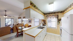 A compact kitchen with white cabinets, a central island, and a dining area with a sofa and chairs. - Pawleys Plantation Greens 1 Bedroom Retreat (Pawleys Island)