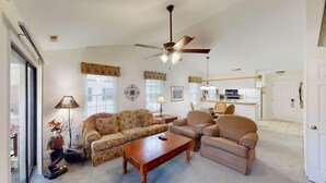 A living room with a sofa, armchairs, a coffee table, a ceiling fan, and a kitchen in the background. - Pawleys Plantation Greens 1 Bedroom Retreat (Pawleys Island)