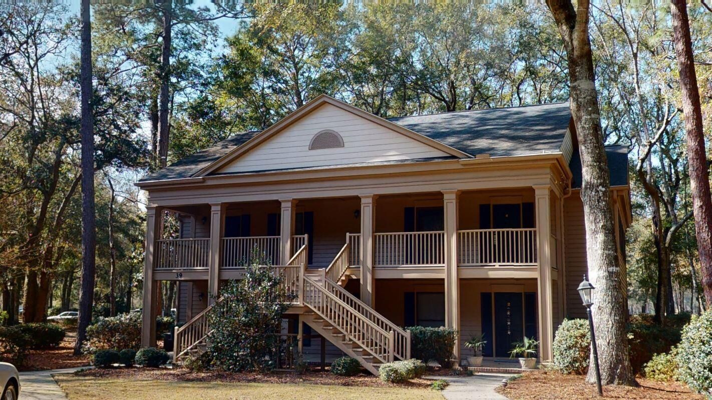 A two-story building with a balcony on the second floor, surrounded by trees.