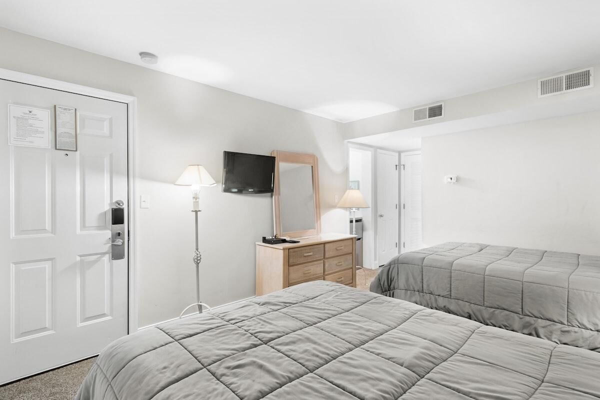 A hotel room with two beds, a dresser, a TV, and a lamp.