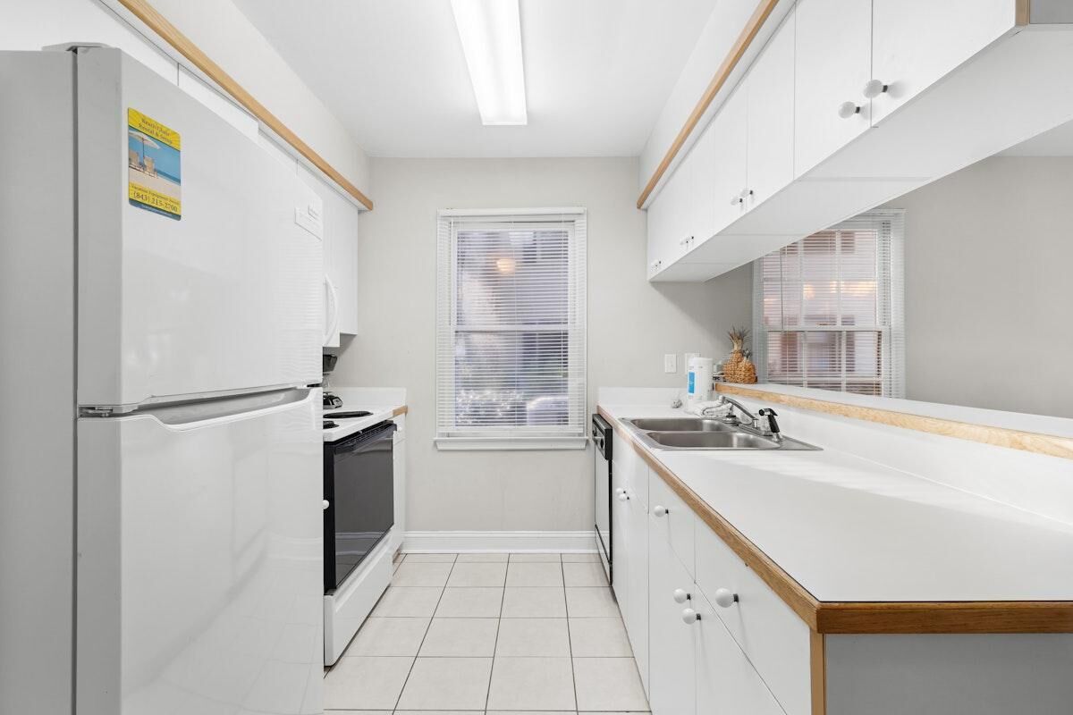 A compact kitchen with white cabinetry, a built-in oven, a sink, and a window with blinds.