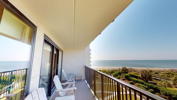 A balcony with white chairs and a view of the beach. - Coastal Hideaway 2 Bedroom Condo with Ocean Views (Pawleys Island)