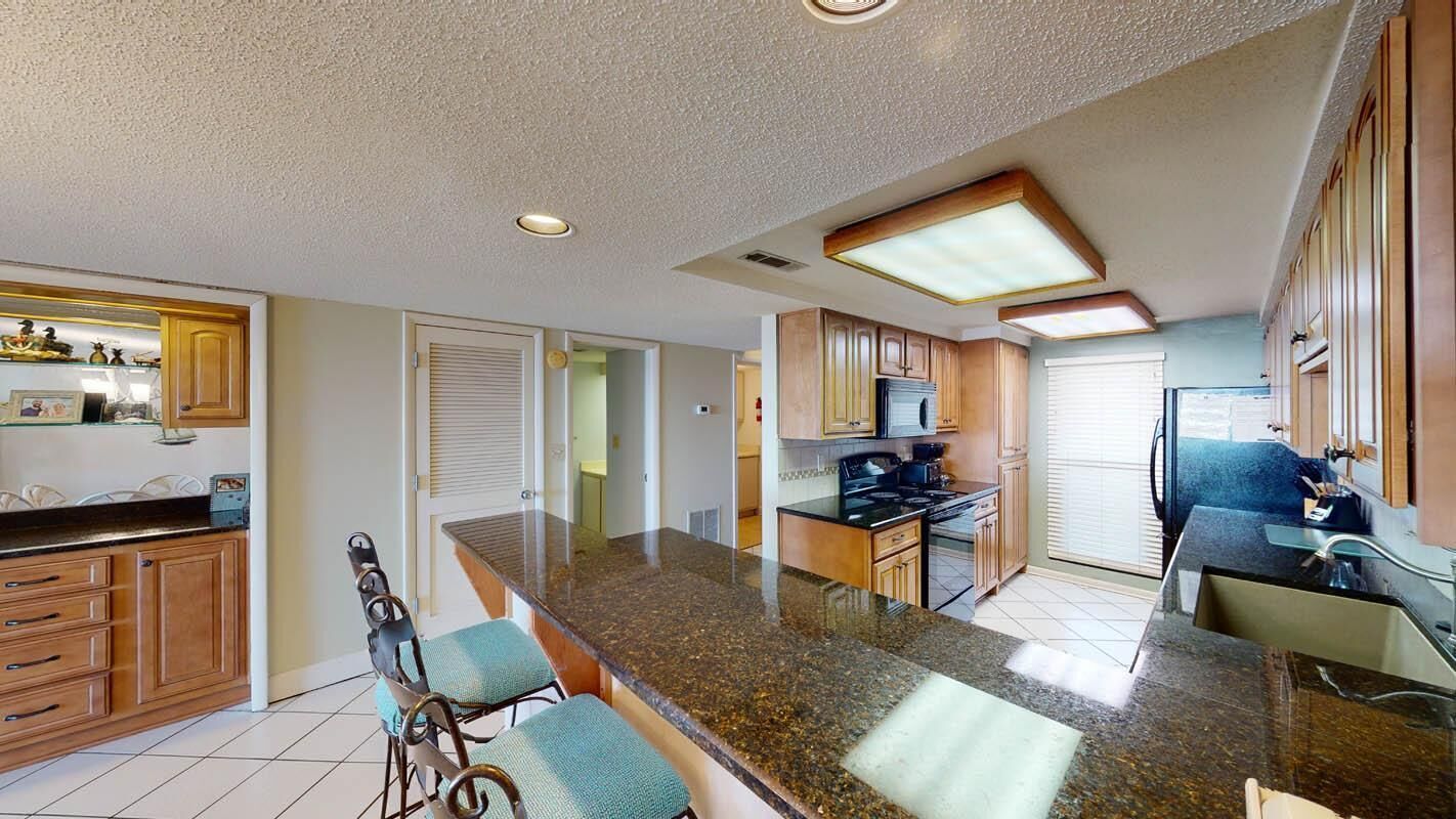 A spacious kitchen with granite countertops, wooden cabinets, and a central island with bar stools.