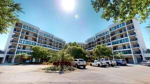 A multi-story hotel with a central courtyard, parking area, and several vehicles. - Coastal Hideaway 2 Bedroom Condo with Ocean Views (Pawleys Island)