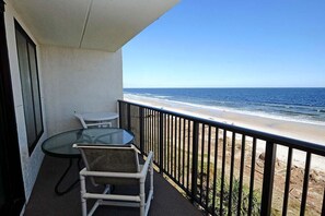 A balcony with a glass table and two chairs, overlooking a beach with a clear view of the ocean. - Seaside Splendor Elegant 2BR Condo Resort Perks (Pawleys Island)