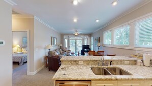 A spacious kitchen with a large island, a dining area with a TV, and a living room with a sofa and a fireplace. - Golf and Beach: 2BR Lakeside Villa with Lake Views (Pawleys Island)