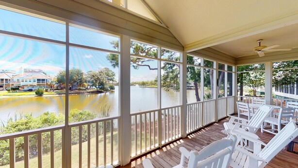A covered porch with white chairs and a view of a lake and buildings. - Golf and Beach: 2BR Lakeside Villa with Lake Views (Pawleys Island)