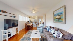 Een ruime woonkamer met een televisie, een witte entertainmentkast, een grijze bank en een schilderij van een boot.