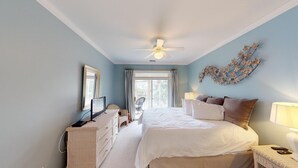 A bedroom with a bed, a ceiling fan, a window, a wall-mounted TV, and a decorative wall piece. - Lake Views, 2BR, 2BA, Lakeside Villa (Pawleys Island)