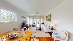 A spacious living room with a wooden dining table, a sofa set, a television, and a ceiling fan. - Lake Views, 2BR, 2BA, Lakeside Villa (Pawleys Island)