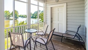 A covered porch with a table and chairs, a bench, and a view of a lake. - Beautiful 2BR 2BA Lakeside Villa with Lake Views (Pawleys Island)