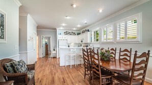 A spacious kitchen with white cabinetry, a dining area with wooden chairs, and a wicker sofa. - Beautiful 2BR 2BA Lakeside Villa with Lake Views (Pawleys Island)