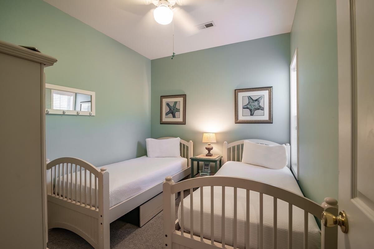 Une chambre avec deux lits simples, une table de chevet avec une lampe et un ventilateur de plafond.