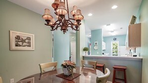 Un coin repas avec une table ronde, des chaises, un lustre et une cuisine en arrière-plan.