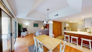 A modern interior with a wooden dining table, white chairs, a kitchen area, and a large window. - Beach and Golf Dreams: 3 Bedroom 2 Bath (Pawleys Island)