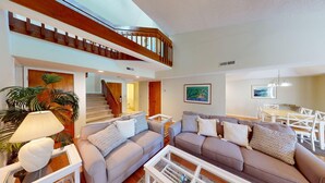 A spacious living room with a high ceiling, a wooden staircase, and a dining area with white furniture. - Beach and Golf Dreams: 3 Bedroom 2 Bath (Pawleys Island)