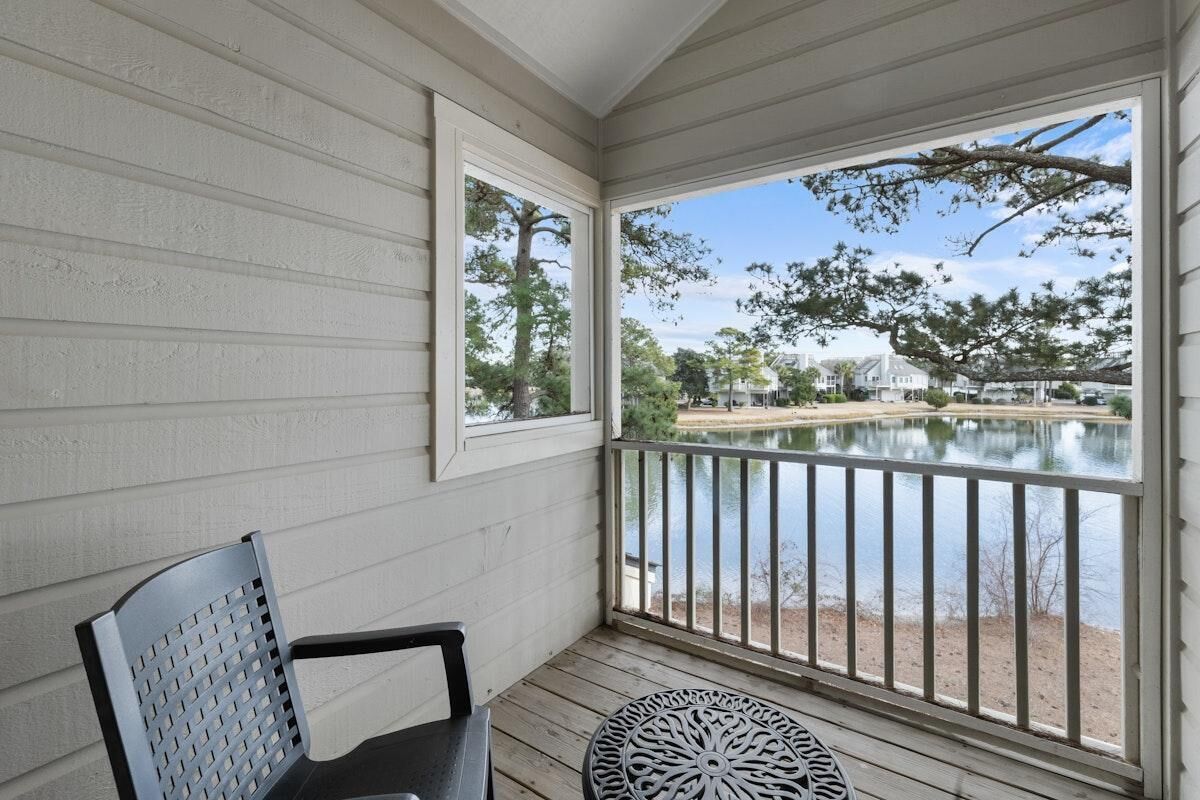 A covered porch with a view of a lake, a chair, and a table.