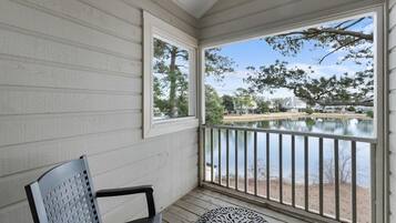 A covered porch with a view of a lake, a chair, and a table.