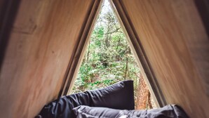 Une tente avec vue sur une forêt, visible à travers une fenêtre triangulaire.