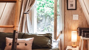 Une chambre confortable avec un lit superposé, une table de chevet avec une lampe, une fenêtre avec des rideaux et une vue sur la verdure à l’extérieur.