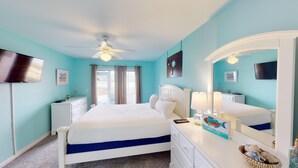 Une chambre à coucher comprenant un lit, une commode, un miroir, un ventilateur de plafond et un téléviseur.