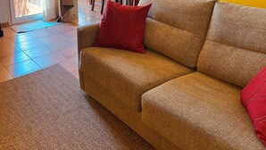 A living room with a sofa, a red pillow, a lamp, and a wall-mounted picture frame. - Sonne, Ruhe, Leuchtend Turkisblaues Wasser und Feinster Sandstrand (Cala Mendia)