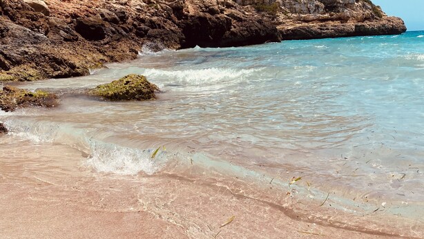 A beach with clear water, rocky cliffs, and greenery. - Sonne, Ruhe, Leuchtend Turkisblaues Wasser und Feinster Sandstrand (Cala Mendia)