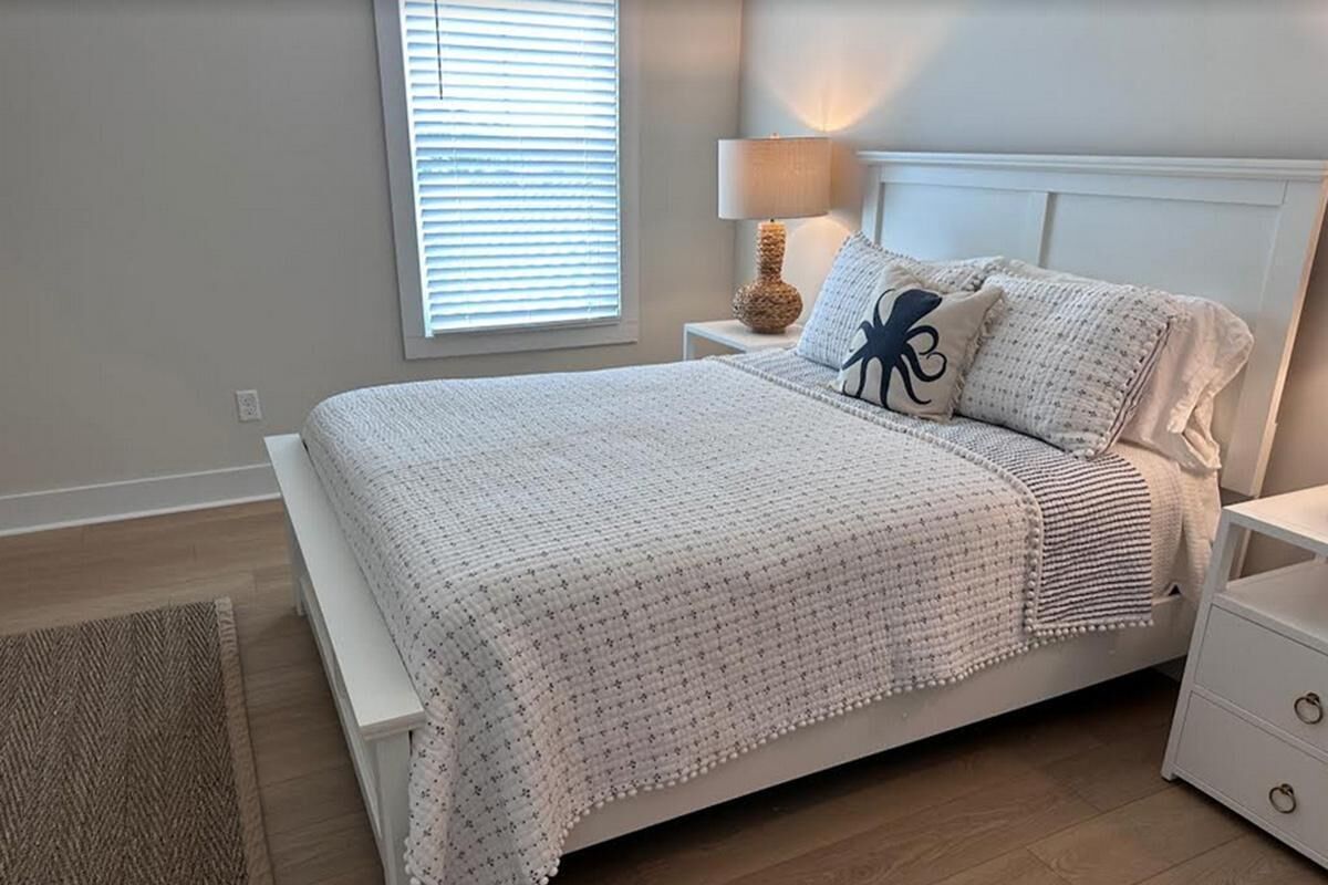 Un dormitorio con cama, mesitas de noche, lámpara y ventana con persianas.
