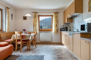 Une cuisine compacte avec des meubles en bois, une table à manger avec des chaises, une fenêtre avec des rideaux et un radiateur.