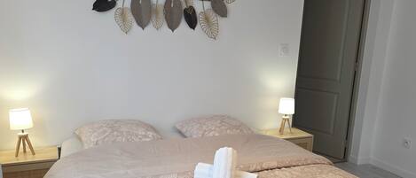 A neatly made bed with a floral-patterned bedspread, two bedside lamps, and a wall decoration of leaves.