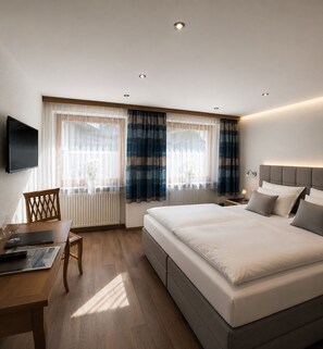 A modern hotel room with a large bed, a desk with a chair, a flat-screen TV, and a window with curtains. - Köcks B 'n B (Galtur)
