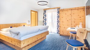 A room with a wooden bed, a desk with a chair, and a large window with curtains. - Köcks B 'n B (Galtur)
