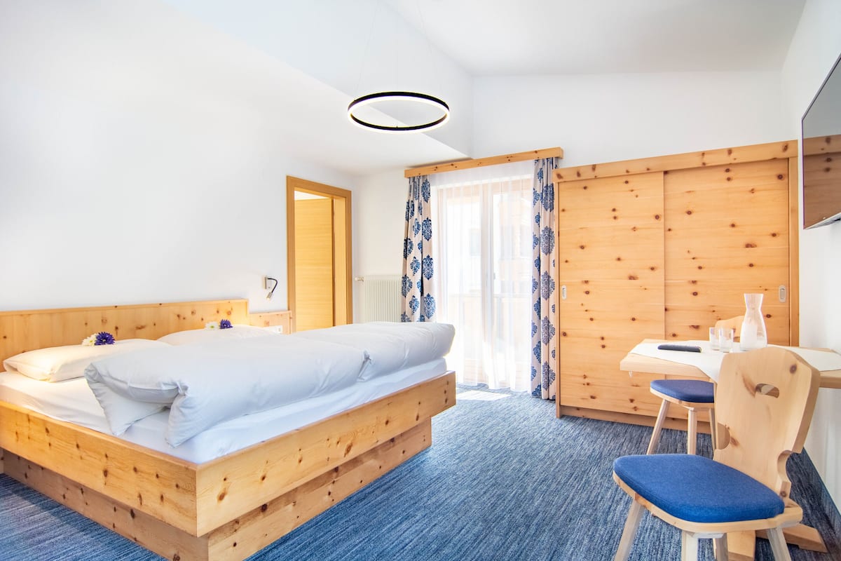 A room with a wooden bed, a desk with a chair, and a large window with curtains.
