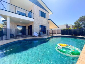 Una casa moderna con piscina, un patio cubierto y un patio trasero cercado.