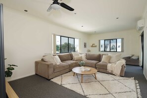 Un salón con un sofá seccional color beige, una mesa de centro redonda y un ventanal con vistas al exterior.