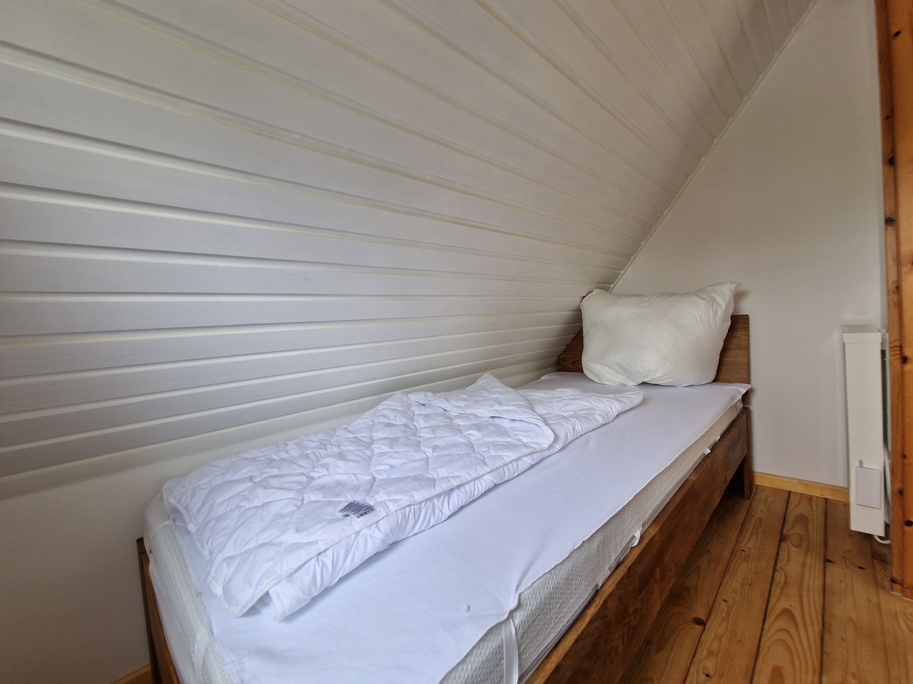 A single bed with white bedding in a room with wooden flooring and white walls.