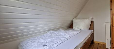 A single bed with white bedding in a room with wooden flooring and white walls.