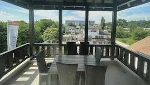 Un espacio de estar al aire libre cubierto, con mesa y sillas, con vistas a un barrio residencial.
