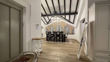 A dining area with a high ceiling, wooden beams, and a chandelier.