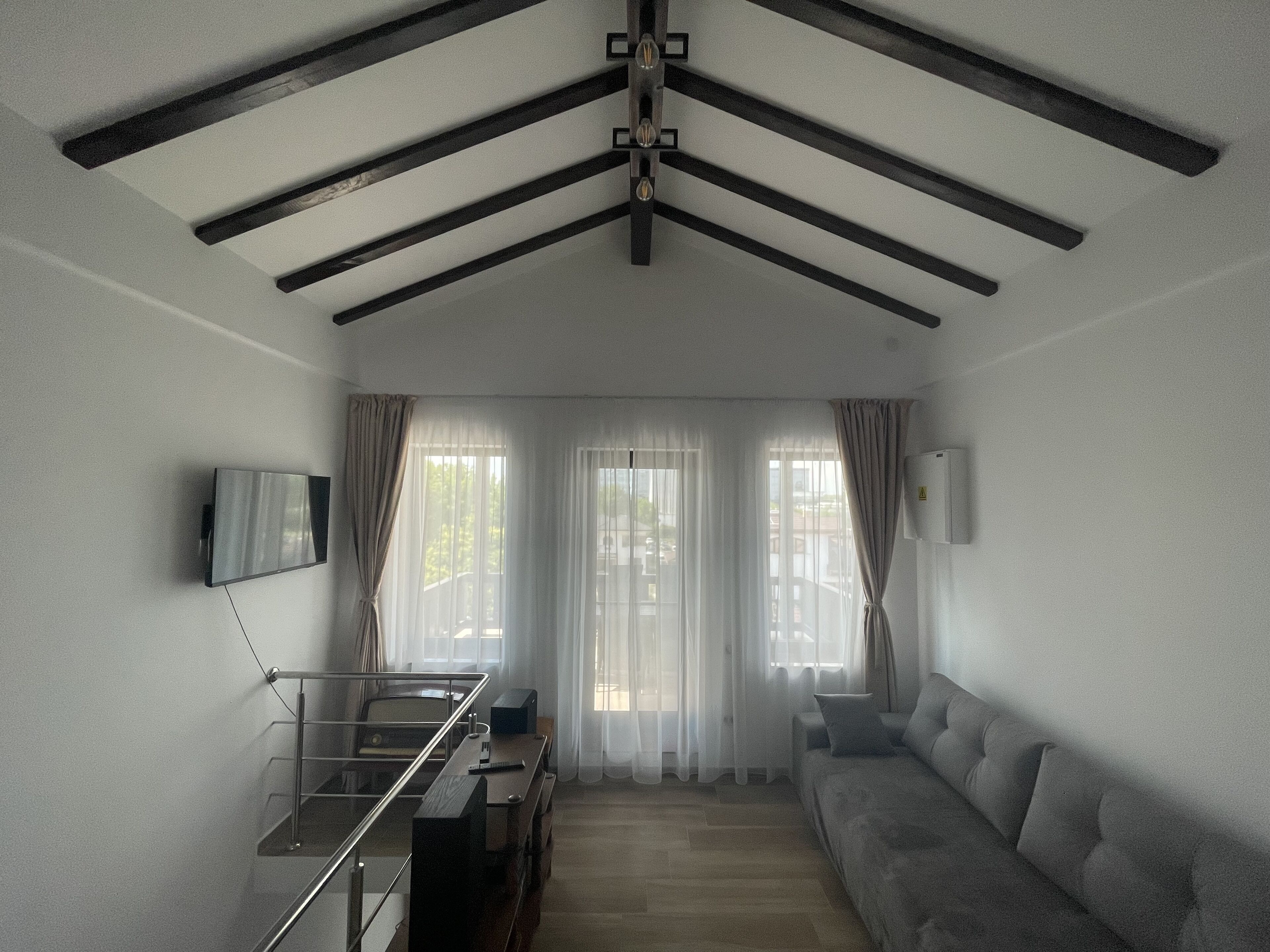 Un salon moderne avec un plafond haut, un canapé, un téléviseur fixé au mur et un coin repas comprenant une table et des chaises.