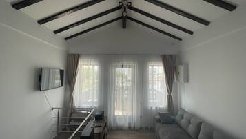 Un salon moderne avec un plafond haut, un canapé, un téléviseur fixé au mur et un coin repas comprenant une table et des chaises.