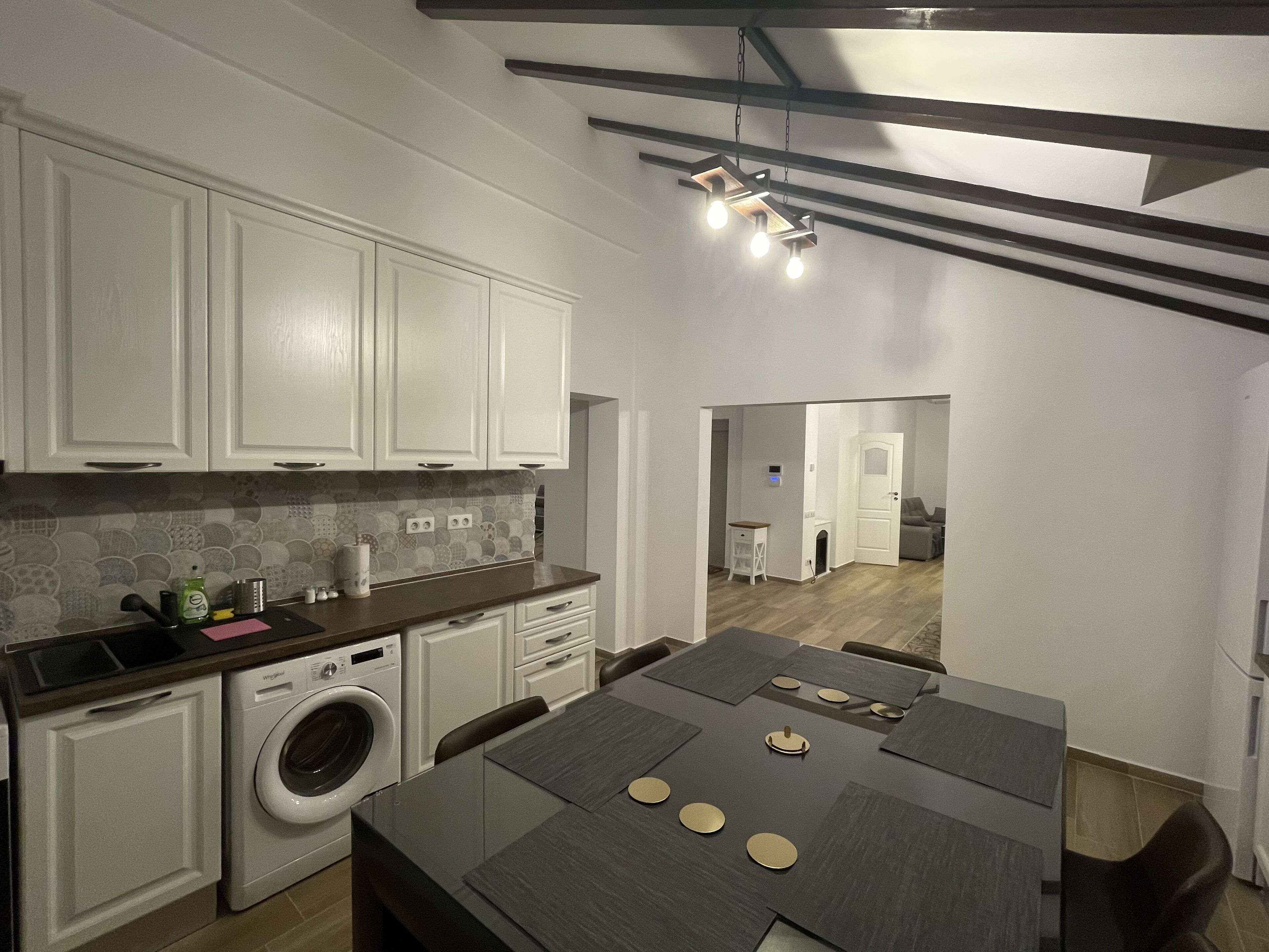 A modern kitchen with white cabinets, a built-in washing machine, and a dining area with a table set for four.